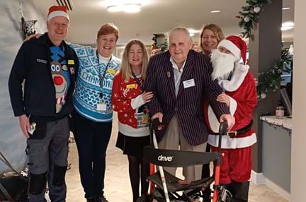 Blind veteran Norman holding a walker surrounded by staff dressed in Christmas jumpers at our new Rustington Centre