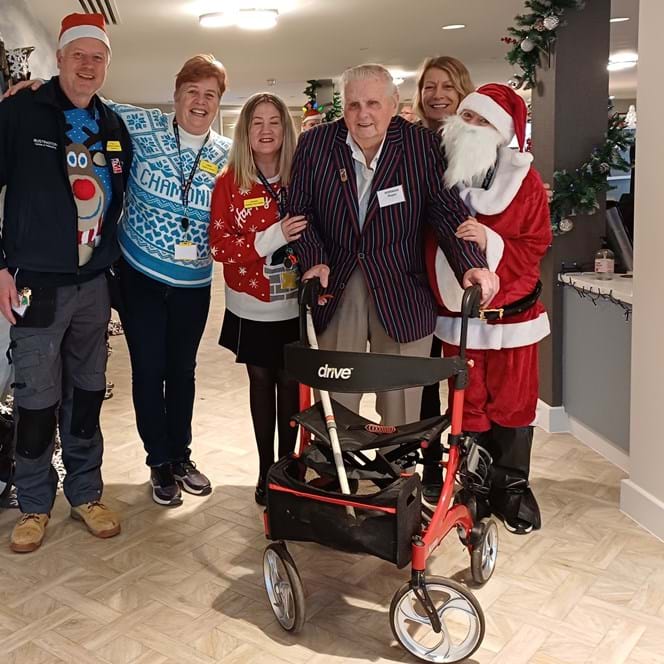 Blind veteran Norman holding a walker surrounded by staff dressed in Christmas jumpers at our new Rustington Centre