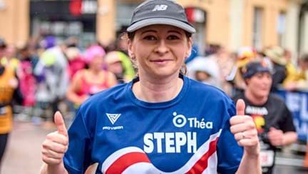 Stephanie running in the London Marathon wearing a Blind Veterans UK T-shirt displaying her name. Steph is smiling with her thumbs up.