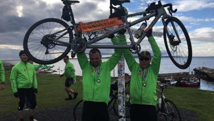 A photo of Craig standing outside holding a tandem bike overhead with his teammate