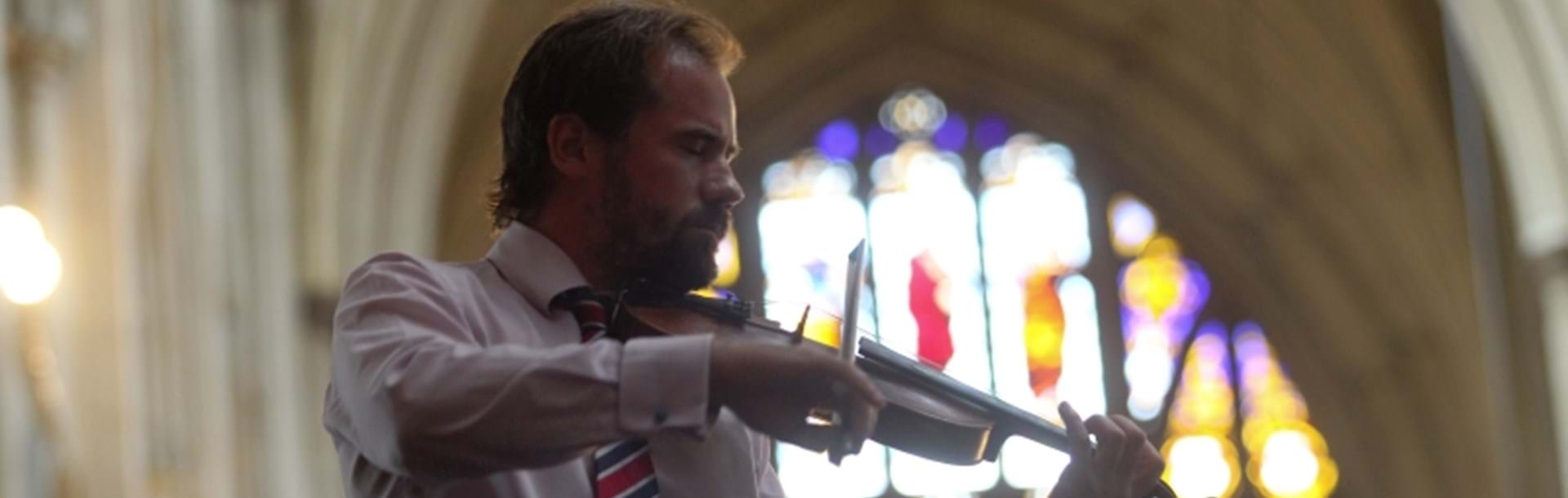 A photo of composer Alastair Caplin playing a violin inside a church