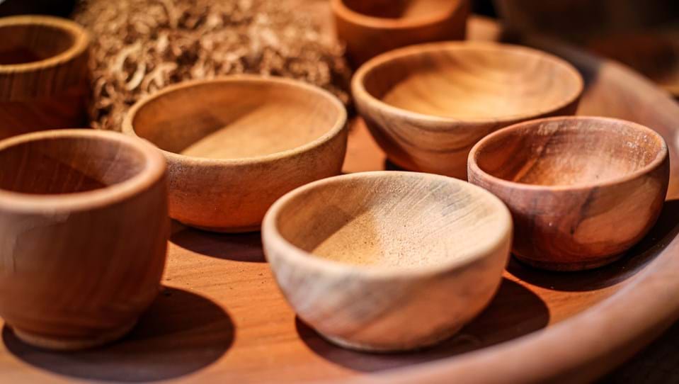 A picture of a wooden tray with wooden bowls on it and wood shaving in the background