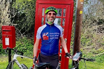 Rob wearing a Blind Veterans UK cycling top stood with his bicycle in front of a red telephone box