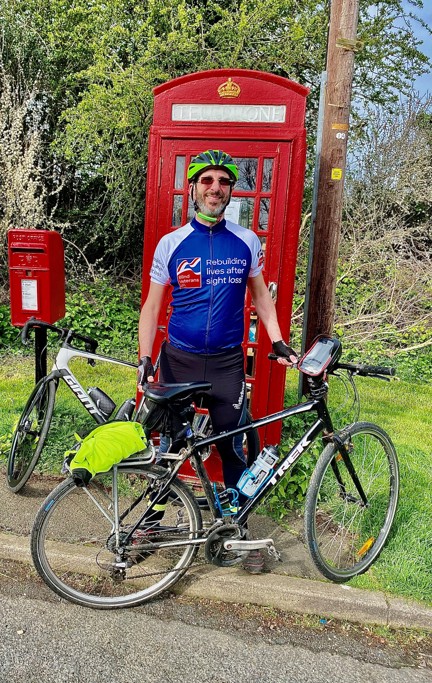 Rob wearing a Blind Veterans UK cycling top stood with his bicycle in front of a red telephone box